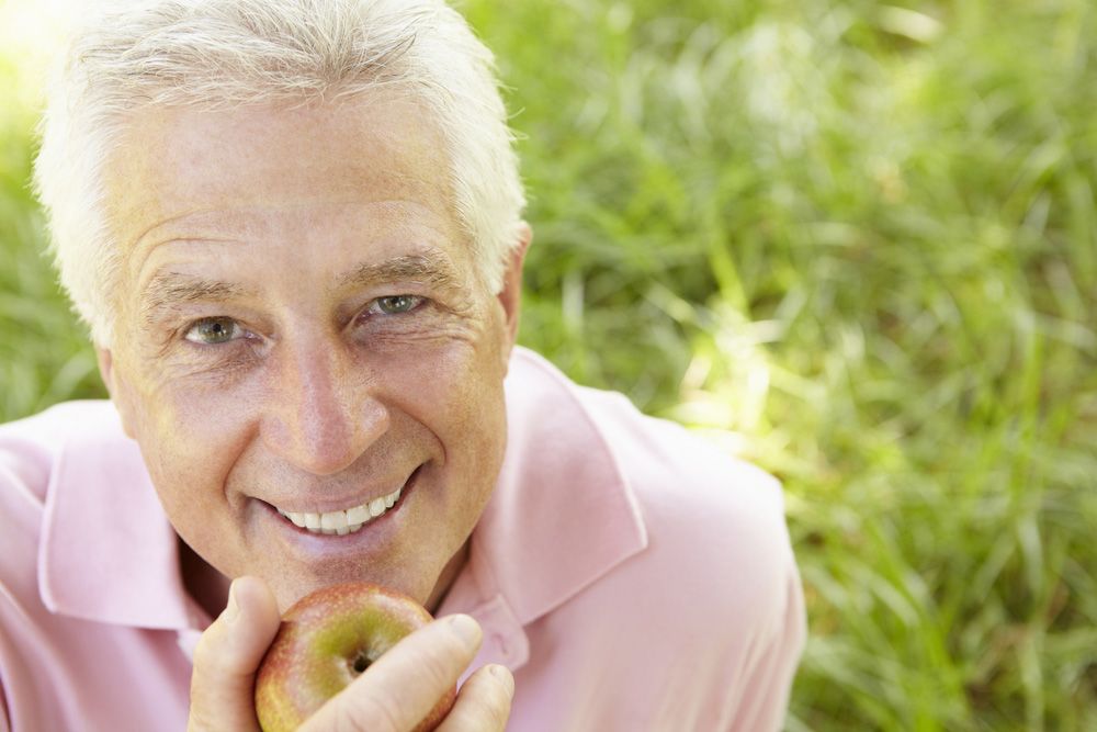 An older man holding up an apple